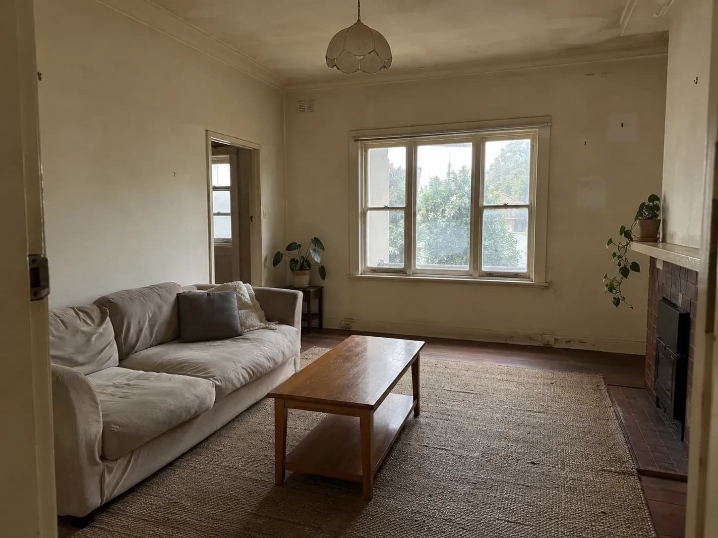 Living room with scuffed, dated cream walls and marked skirting boards