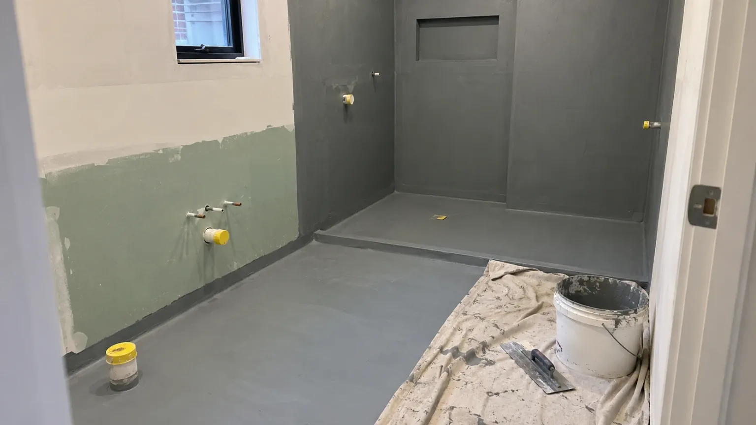 Bathroom mid-renovation with waterproofing membrane applied before tiling