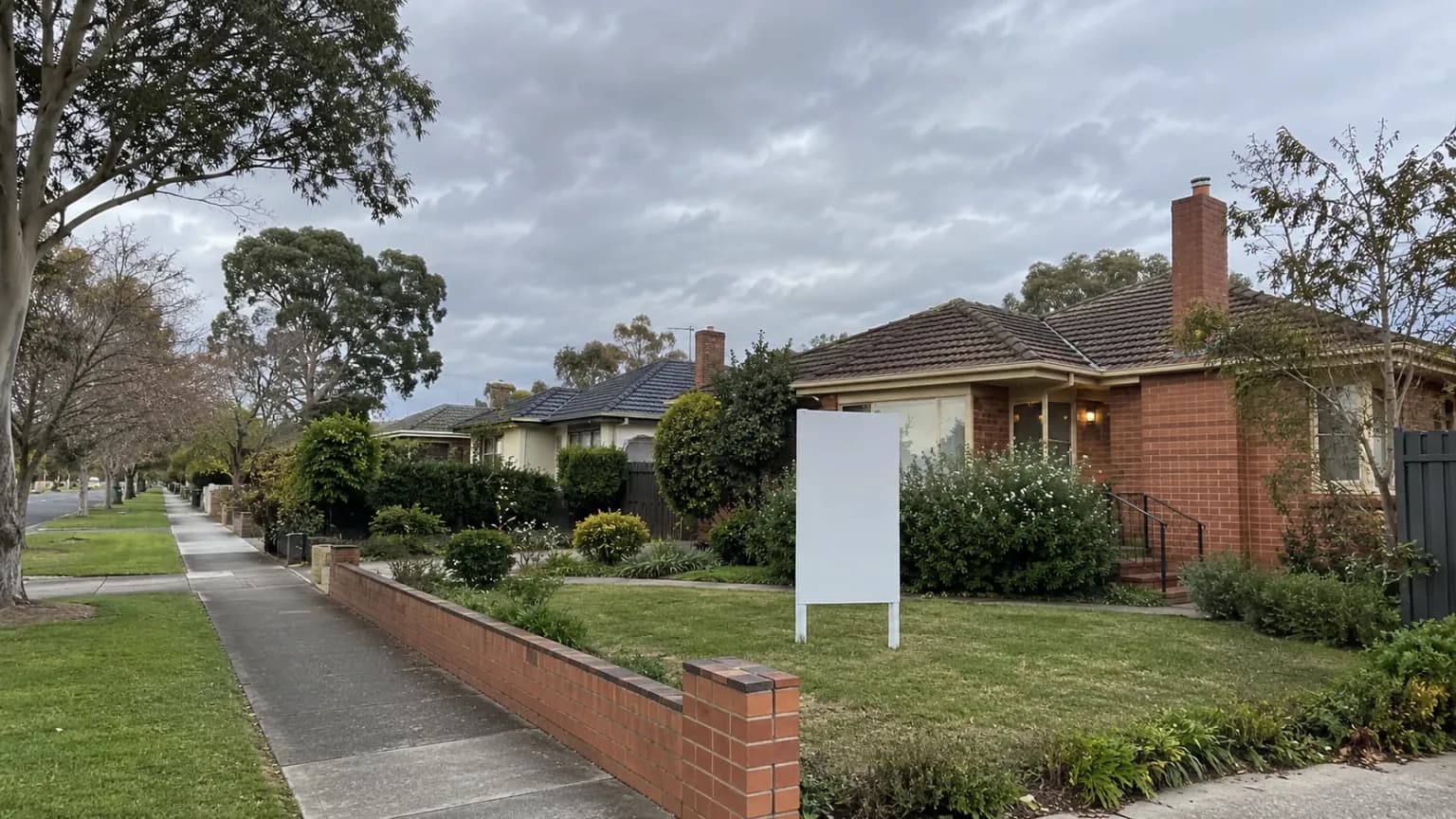 Suburban street with a blank for-sale board outside a family home