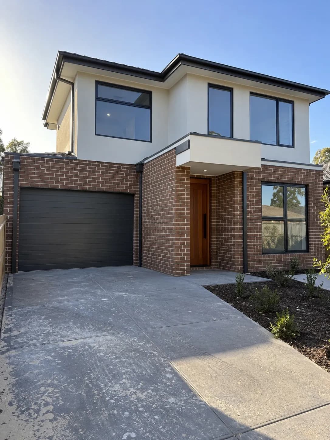 Front of a new double-storey home with rendered upper level and timber entry door